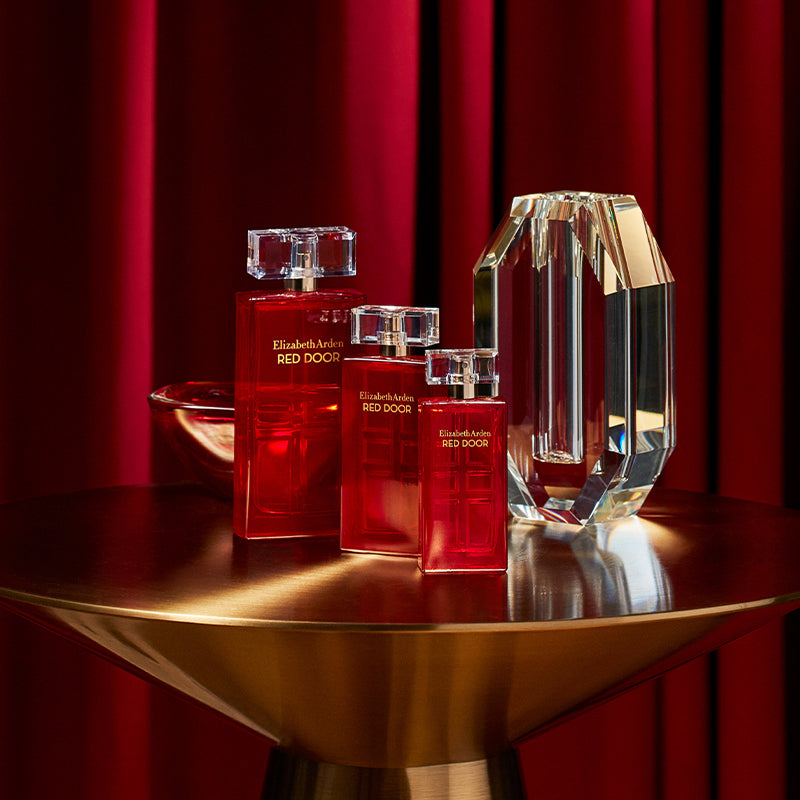 Red Door perfume bottles by Elizabeth Arden on a gold table with a red curtain background