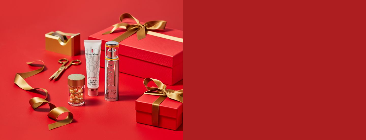 Red gift box with gold ribbon, skincare products, and scissors on a red background