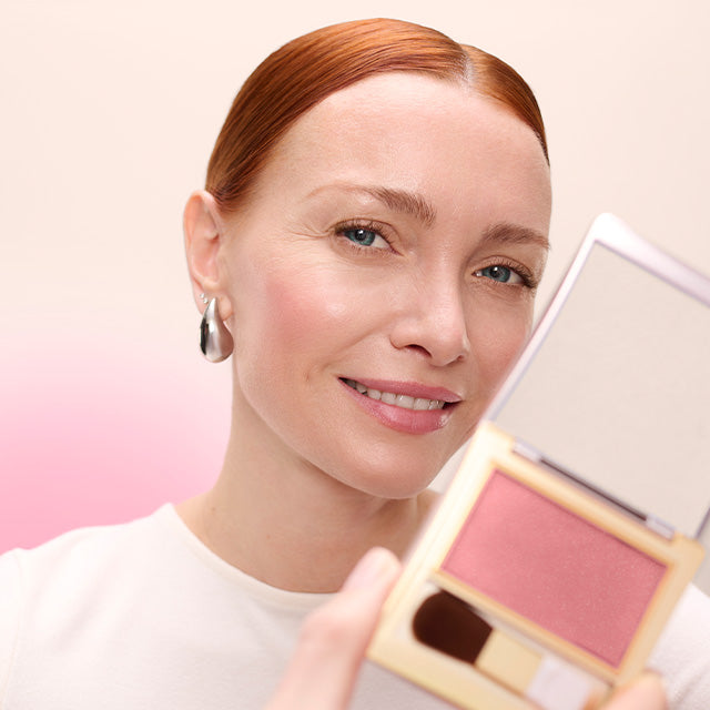 Model with blush on her cheeks and holding the blush product